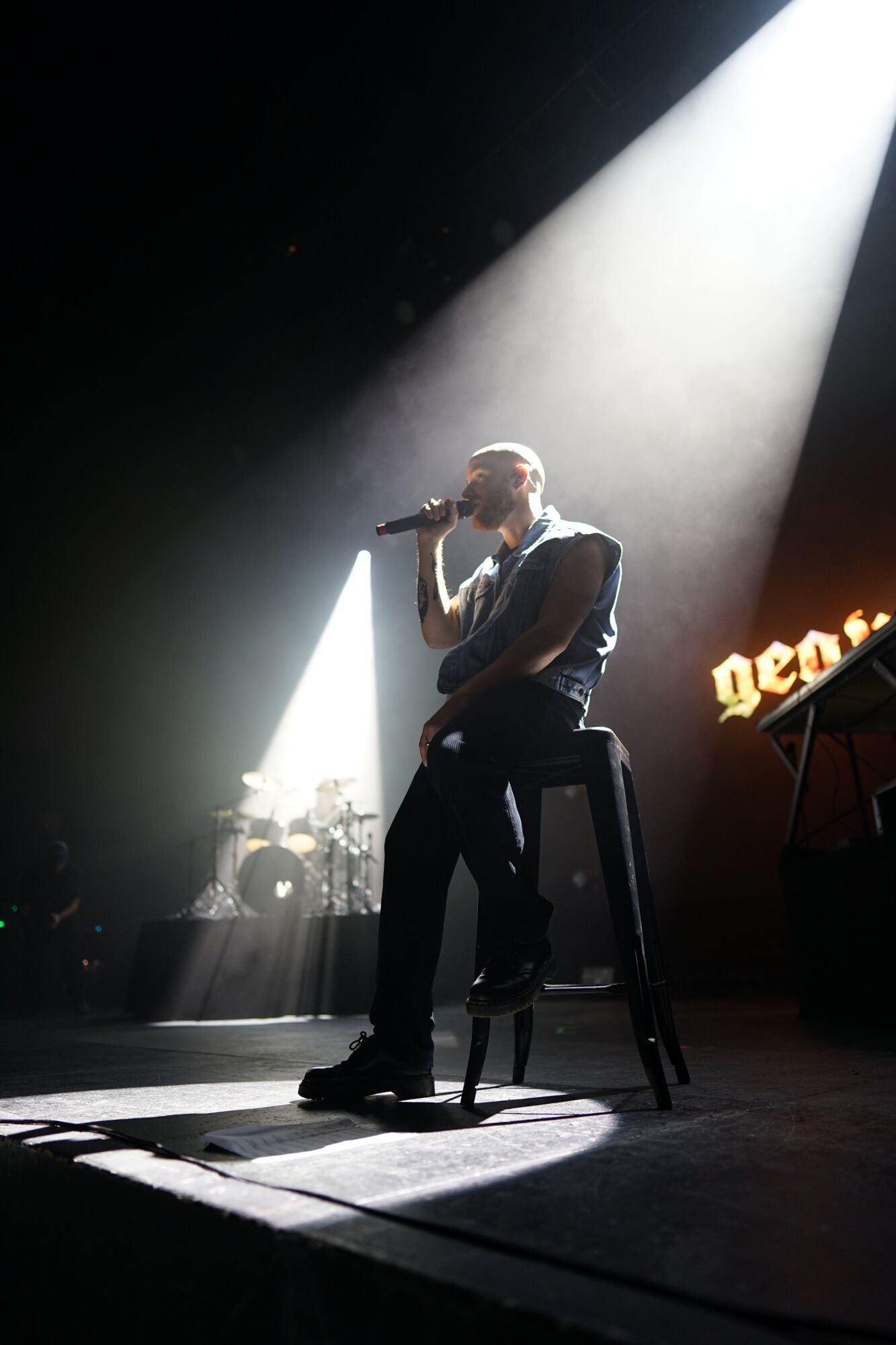 Chanteur assis sur un tabouret sous un faisceau de lumière blanche
