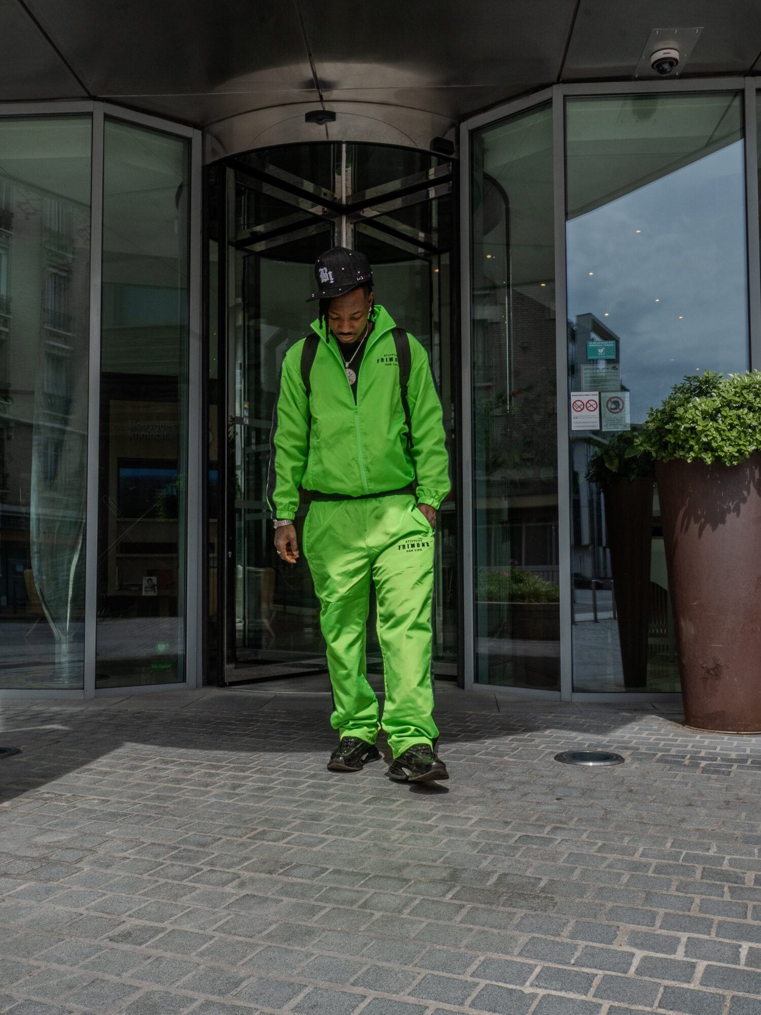 Homme en survêtement vert fluo devant une porte tambour vitrée, shooting streetwear pour OG Shark